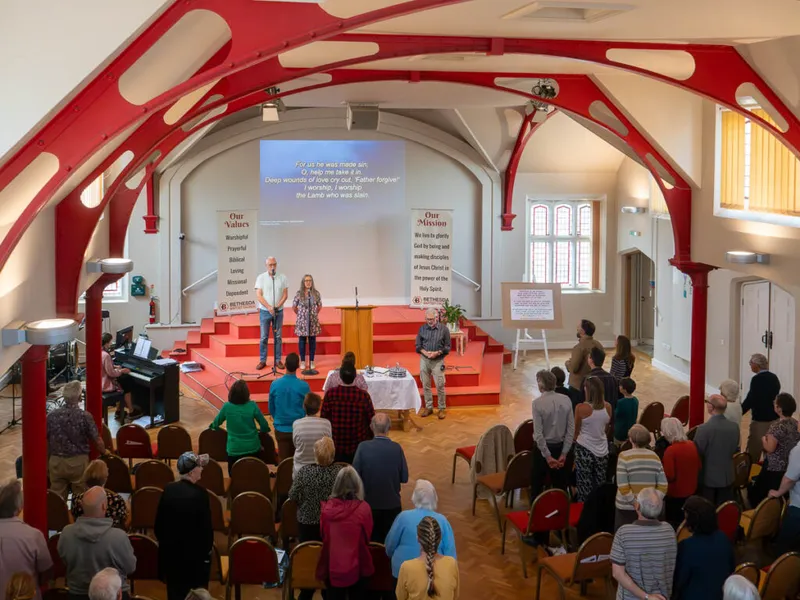 A Sunday service in the main hall at Bethesda, the church family standing to sing beneath the red iron arches